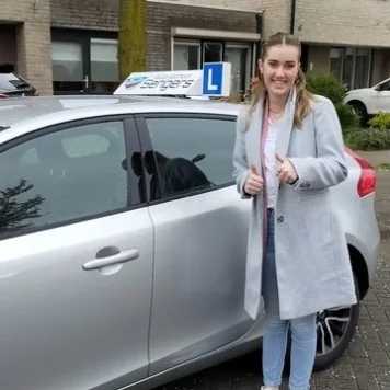 Geslaagde leerling met duim omhoog bij de lesauto van Autorijschool Sengers