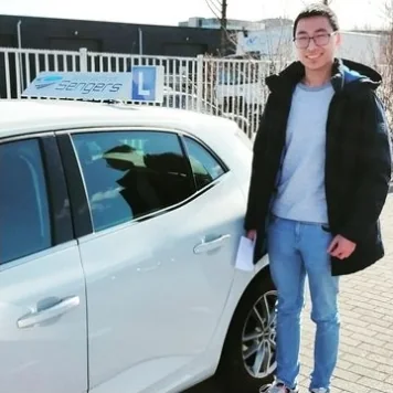 Geslaagde leerling met het examenformulier naast de lesauto van Autorijschool Sengers