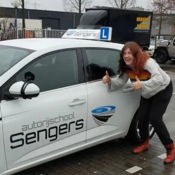 Geslaagde leerling met duimen omhoog naast de lesauto van Autorijschool Sengers