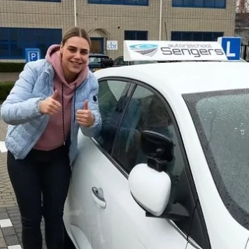 Geslaagde leerling met duimen omhoog bij de lesauto van Autorijschool Sengers